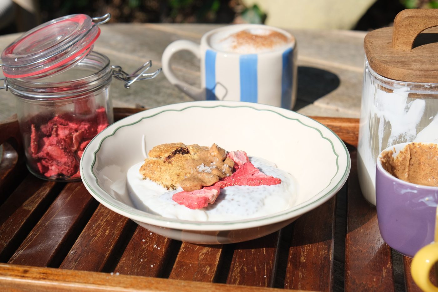 Ontbijt met Millit, chiapudding en cappuccino op een houten dienblad in de zon